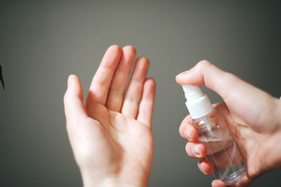 Close-up of woman hand holding bottle against gray background