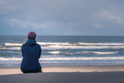 Rear view of woman standing at beach against cloudy sky