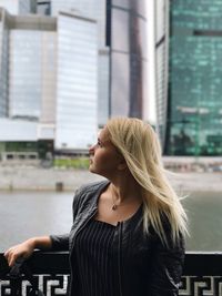 Thoughtful woman standing by railing against buildings in city