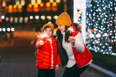 A beautiful boy and his mother celebrate new year or christmas with sparklers on the background 