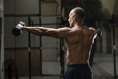 Shirtless man holding dumbbells in gym