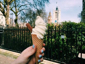 Cropped image of woman hand holding ice cream cone on footpath against big ben