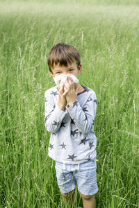 Portrait of boy covering face while standing on field