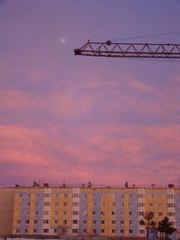 Low angle view of crane by building against sky during sunset