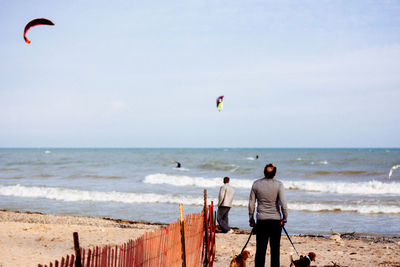 Rear view of man with dogs standing at beach against sky