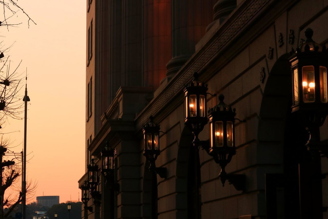LOW ANGLE VIEW OF ILLUMINATED STREET LIGHT AGAINST BUILDINGS AT SUNSET
