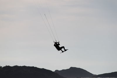 Low angle view of silhouette person kiteboarding on sea against cloudy sky