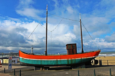 Old boat on footpath by beach against cloudy sky