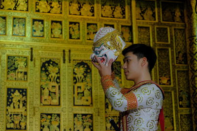 Side view of boy holding painting standing against wall