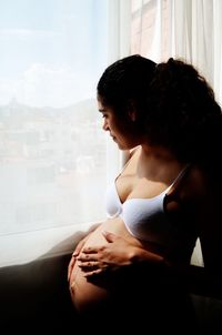 Side view of young woman looking down while standing against window