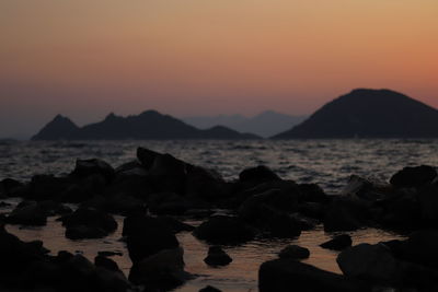 Rocks on beach against sky during sunset