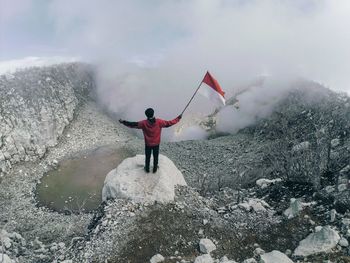 Rear view of man holding flag while standing on mountain