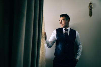 Thoughtful businessman holding curtain at home