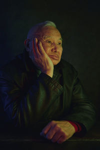 Pensive senior man sitting with hand on chin against black background