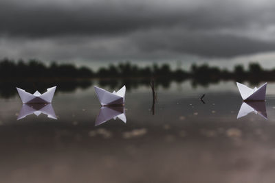 Paper boats in lake against cloudy sky