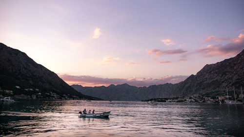 Boats moored on sea against mountains during sunset