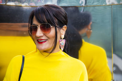 Fashionable mature woman wearing yellow top and sunglasses in city