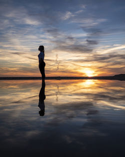 Full length of silhouette woman standing on shore against sky during sunset