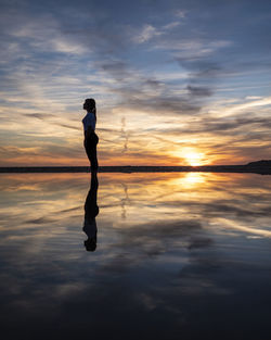 Silhouette man standing on shore against sky during sunset