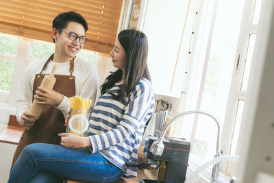 Woman with man holding uncooked pasta jar in kitchen at home