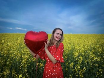 Portrait of young woman standing on field against sky