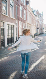 Rear view of woman standing on footpath amidst buildings