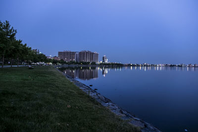 Scenic view of river by illuminated buildings against clear blue sky