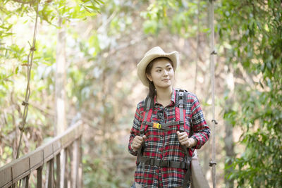 Woman looking away while standing on footbridge against trees in forest