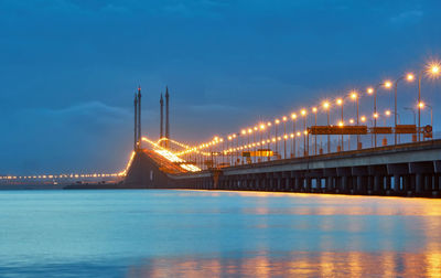 Illuminated bridge over lake against cloudy sky at dusk