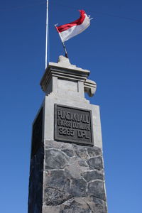 Low angle view of flag against building against clear blue sky