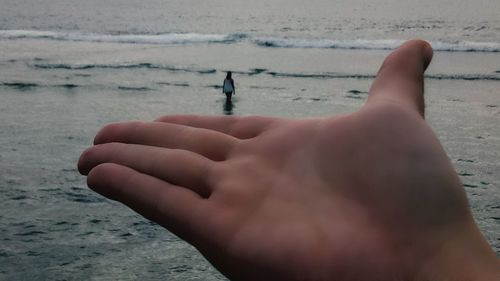 Close-up of hands on sea against sky