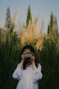 Portrait of woman photographing against plants