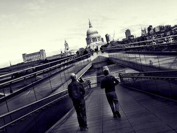 People walking on bridge in city against sky