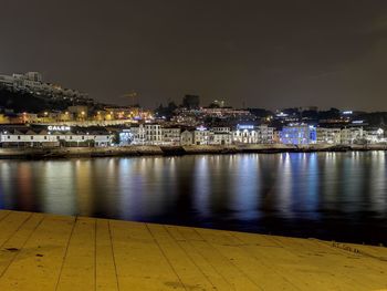 Illuminated buildings by river against sky at night