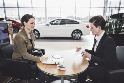 Saleswoman showing document to customer at desk in car showroom