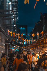 People on illuminated street amidst buildings in city at night