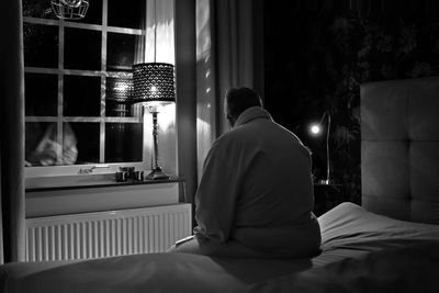 Rear view of man sitting on bed at home