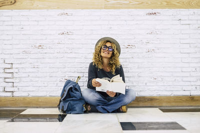 Full length of woman reading book sitting against wall