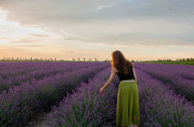 Rear view of woman standing on field against cloudy sky