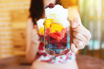 Unrecognizable woman holding and showing a jar with chopped fruit salad. mango, apple, grapes