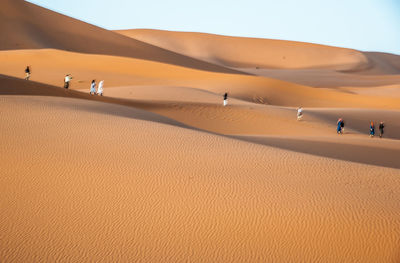 People on sand dune in desert against sky