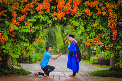 Man proposing woman on footpath amidst trees