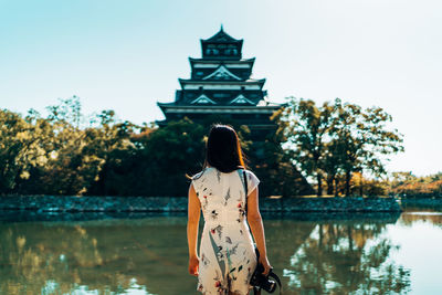 Rear view of woman standing by lake against sky