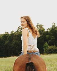 Portrait of beautiful smiling young woman riding brown horse on field