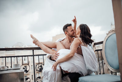 Young couple kissing on railing against sky