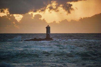 Lighthouse by sea against sky during sunset