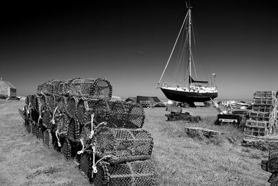 Stack of creels by boat on field against sky