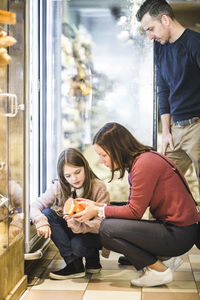 Father looking at daughter and woman choosing food by refrigerator in supermarket