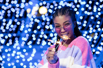 Cheerful black woman with braided hairstyle and pink glasses enjoying christmas lights