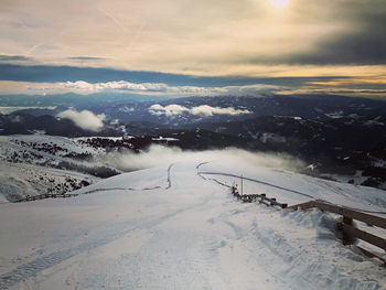 Snow covered land against sky during sunset